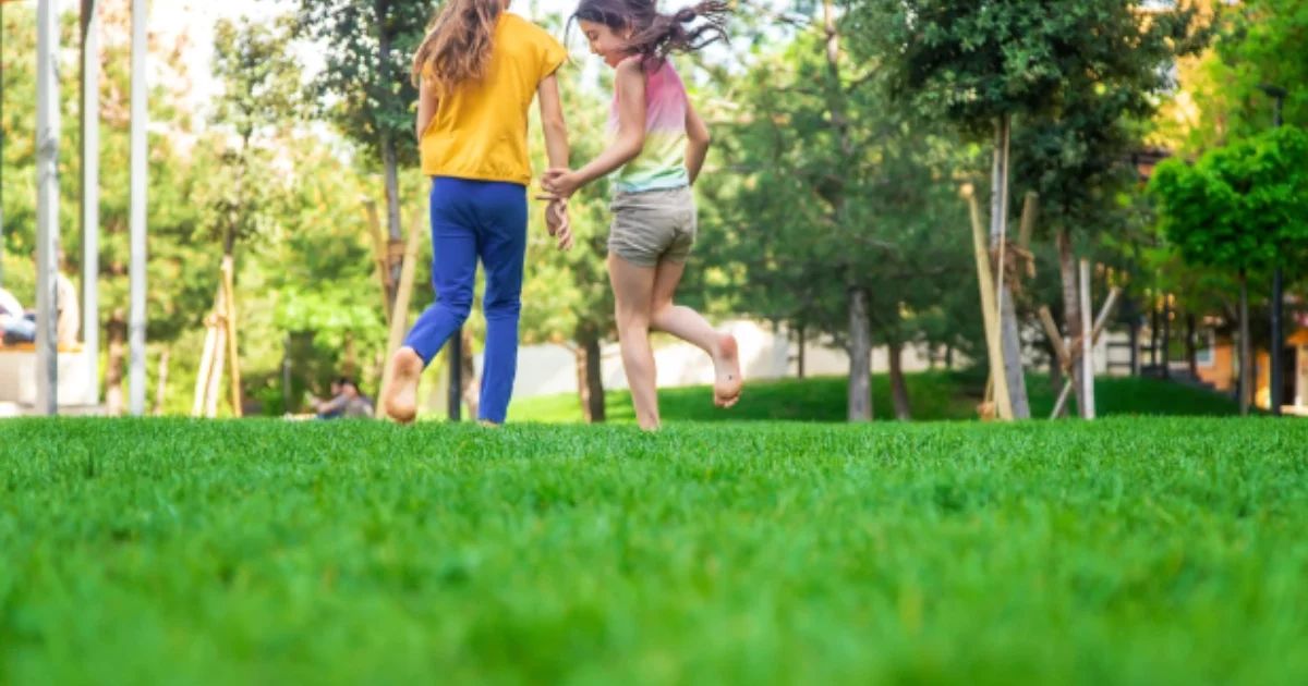 Two girls running barefoot on green grass in a park.